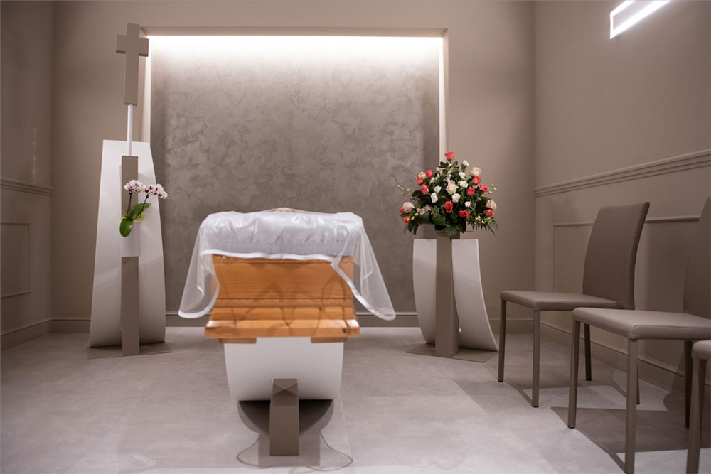 stanza per veglia funebre allestita con fiori e sedute e una bara al centro