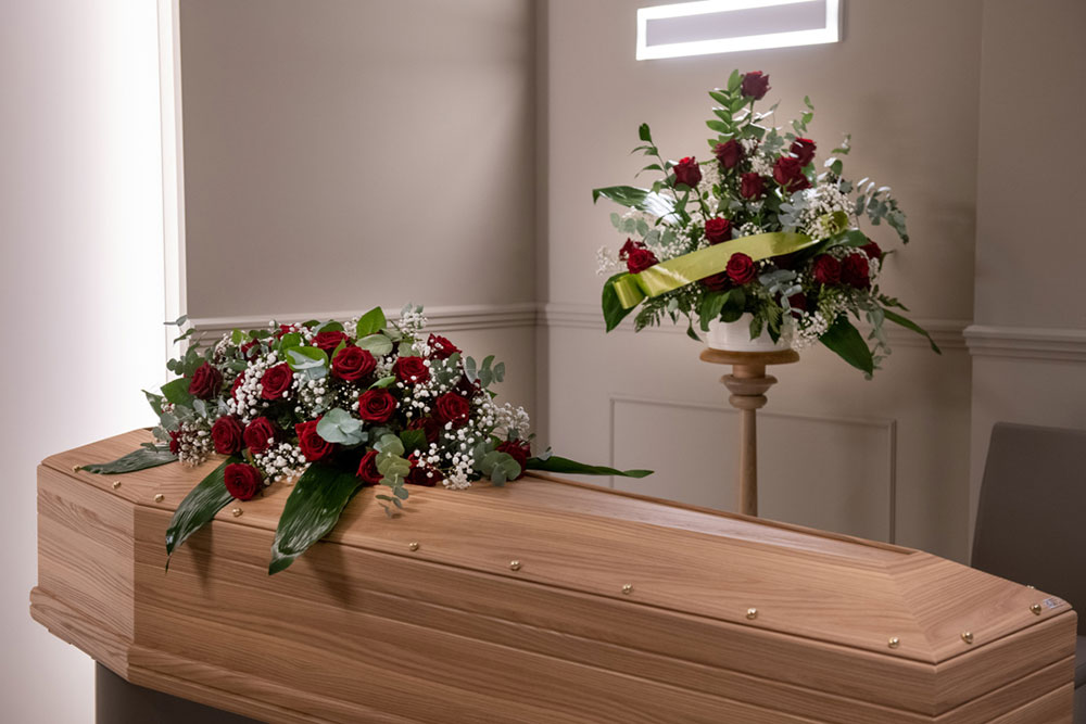 bara in legno chiaro con sopra rose rosse e gypsophila bianca in una camera funeraria